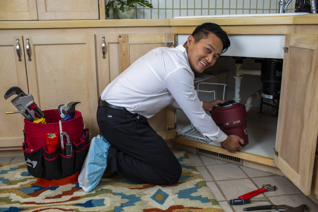 Plumber installing a new garbage disposal under a kitchen sink