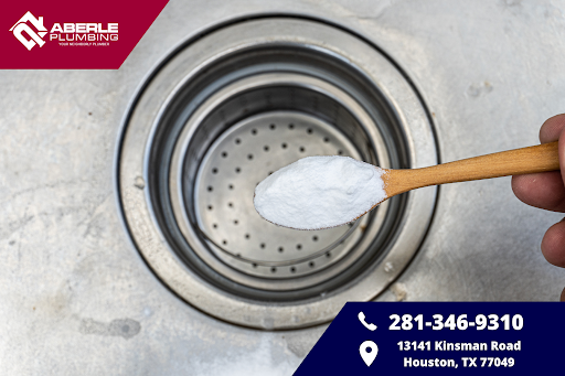 Hand holding a spoon of baking soda on top of sink with a clogged drain.