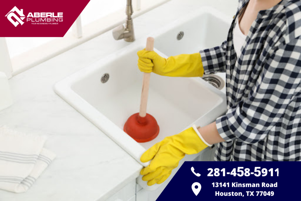 A woman wearing gloves while plunging a clogged kitchen sink.