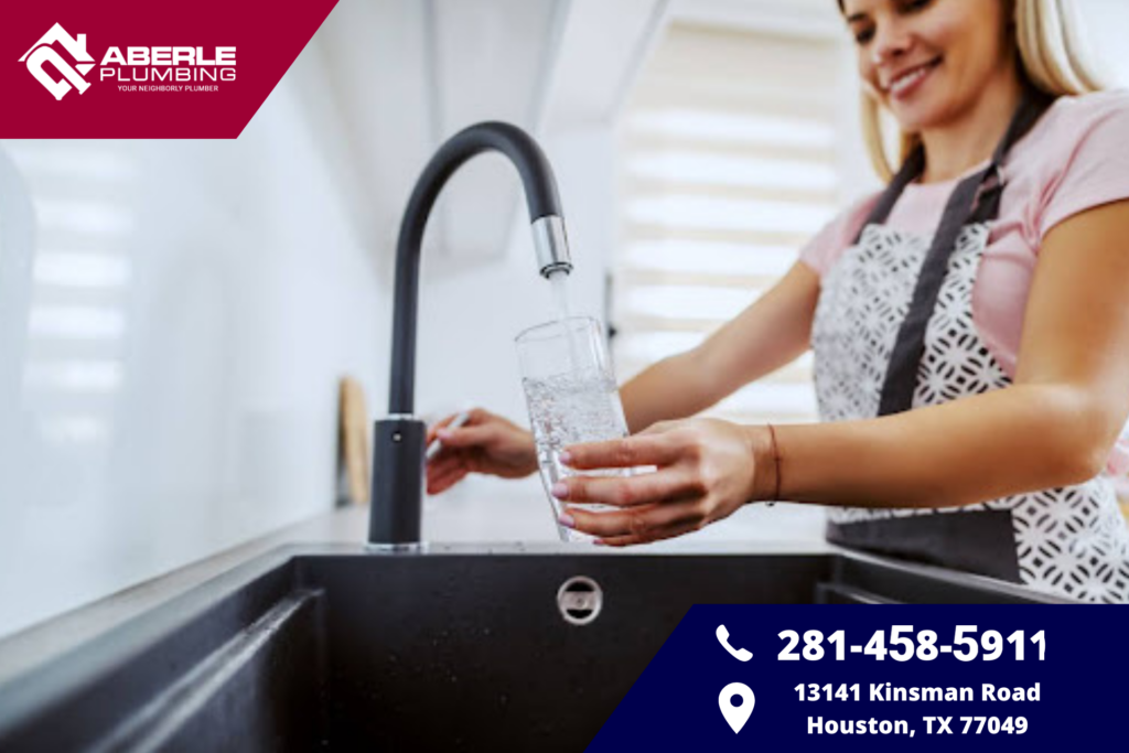 A woman filling a water glass at a kitchen sink.